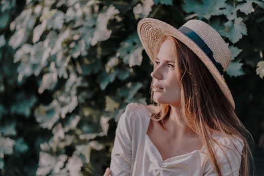 Woman with straw hat stands in front of vineyard. She is wearing a light dress and posing for a photo. Travel concept to different countries.