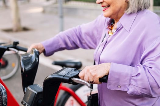 unrecognizable senior woman taking rental bike from parking row, concept of sustainable mobility and active lifestyle in elderly people