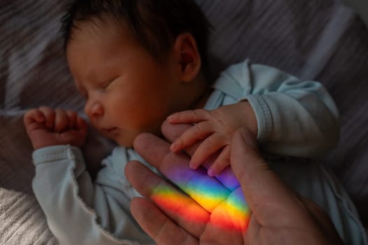 A man holds his newborn son's hand. Beam of light through a prism