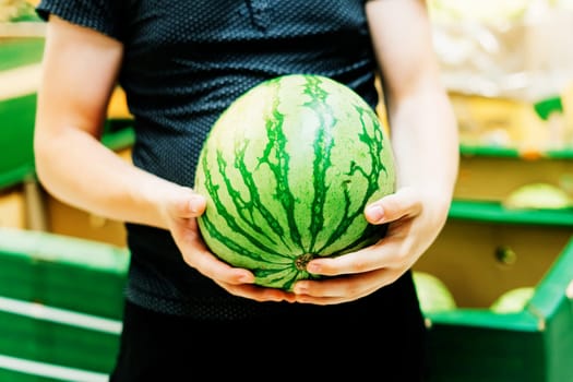 Hand is holding watermelon from the supermarket shelf, close up photo
