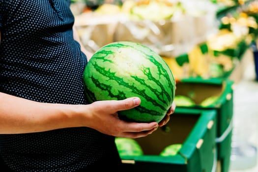 Hand is holding watermelon from the supermarket shelf, close up photo