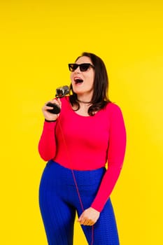 Woman in sport clothes sings into wired microphone and claps her hands on a yellow background