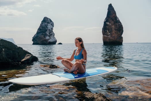 Woman sup yoga. Middle age sporty woman practising yoga pilates on paddle sup surfboard. Female stretching doing workout on sea water. Modern individual hipster outdoor summer sport activity