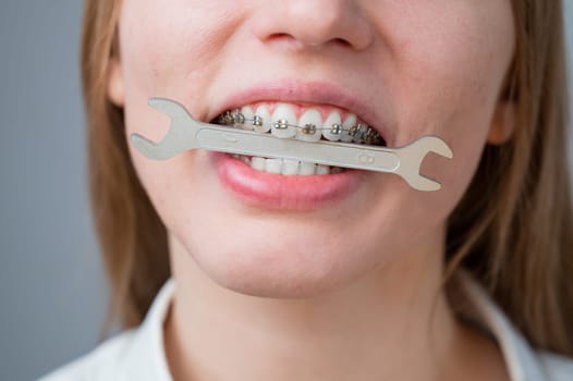 Close-up portrait of a woman with braces holding a wrench in her teeth