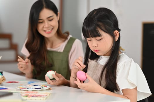 Little child girl painting Easter eggs with her mother in living room. People, holiday and activity concept