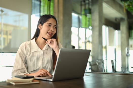 Attractive millennial businesswoman using laptop on wooden table.