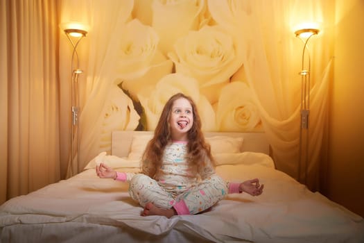 Happy small young child girl doing yoga in hotel or in bed room
