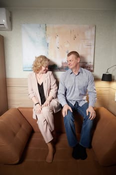 Loving adult couple communicates and embraces privately in the living room or in hotel. Woman is wearing business formal suit and man is wearing jeans and a shirt, indicating a close relationship