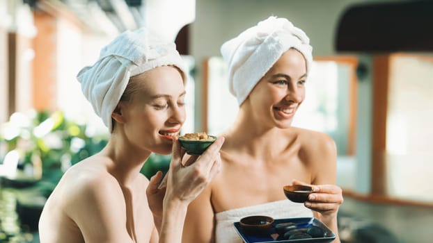 Couple of beautiful woman interested in homemade facial masks while sitting at spa salon. Attractive woman in white towel enjoy herbal masks with her friend surrounded by nature. Tranquility.