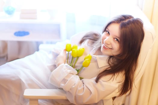Beautiful sweet girl in nightgown in early morning with bouquet of delicate yellow tulips. Gift on International Women's Day on March 8th. Cosmetics, skin and hair care. Perfume, natural fragrance