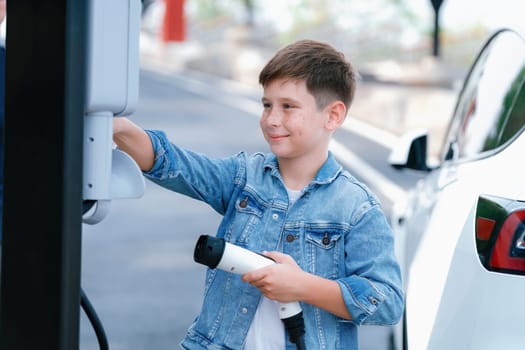 Little boy recharging eco-friendly electric car from EV charging station. EV car road trip travel concept for alternative transportation powered by clean renewable and sustainable energy. Perpetual