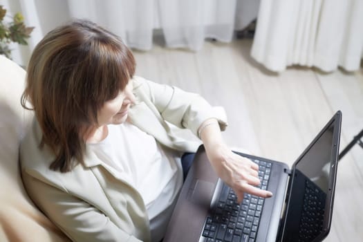 Elderly lady with a laptop in the room. A businesswoman is a leader, a manager is working. Grandma communicates with her grandchildren on the Internet