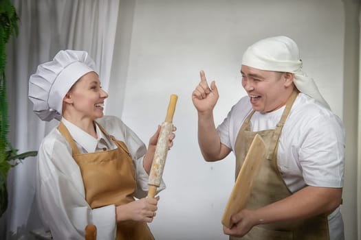 Cute oriental family with wife and husband cooking in kitchen on Ramadan, Kurban-Bairam, Eid al-Adha. Funny fighting parents at cook photo shoot. Pancakes, pastries, Maslenitsa, Easter