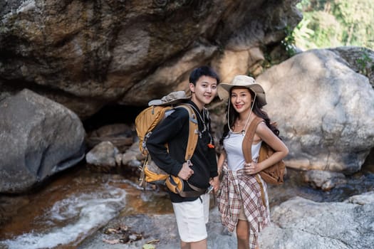 Happy LGBT Lesbian couple Travelers Hiking with Backpacks in waterfall Trail. LGBT Lesbian Couple Hikers with backpacks walks in mountains in vacation.