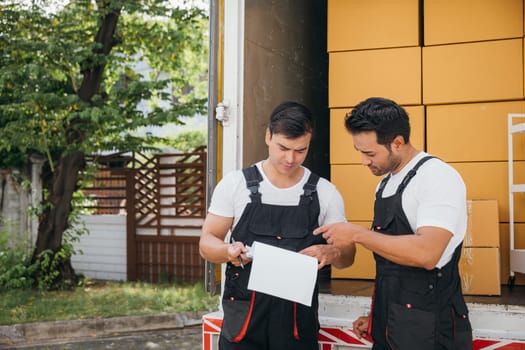 A delivery man unloads boxes while a coworker documents on clipboard by the truck. Removal company's teamwork ensures efficient transportation for relocation. Moving Day