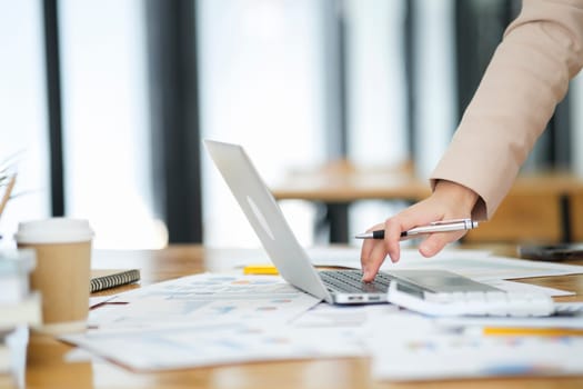 Close-up of a businesswoman hand as she meticulously analyzes data on her laptop, surrounded by business charts and a calculator..