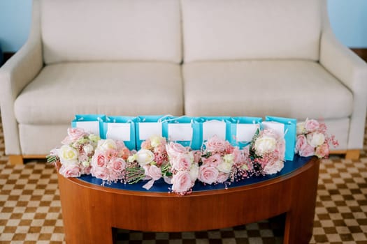 Small bouquets of pink roses lie on the table near blue gift bags in the room. High quality photo