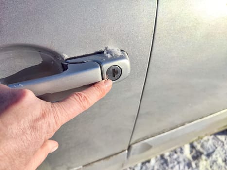 Frozen Car Lock on Cold Winter Day. Woman person attempts to unlock a frozen car door, showing the challenges faced during the cold winter months when car locks freeze
