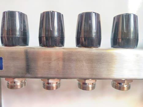 Close-up of plastic taps, valves, regulators on underfloor heating pipes and water standing in a row