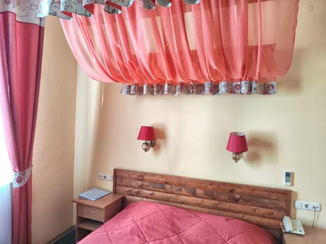 Small compact stylish bedroom in stylish soothing With double bed with red bedspread and a canopy. Concept of small cozy bedroom or hotel room