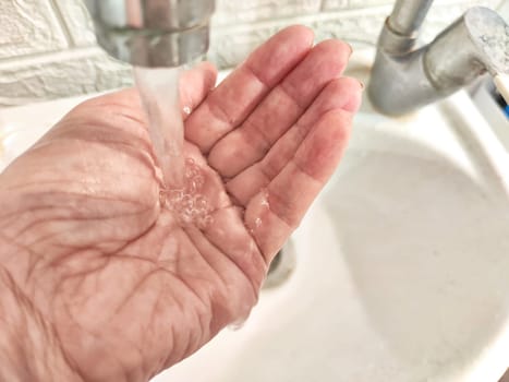 Water Flowing Onto an Open Hand in a Sink. detailed view of a stream of clear water pouring down onto the palm of hand. Concept of hygiene or the sensual pleasure