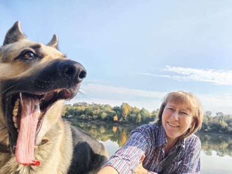 Adult girl with shepherd dog taking selfie in forest. Middle aged woman and big shepherd dog on nature. Friendship, love, fun, hugs