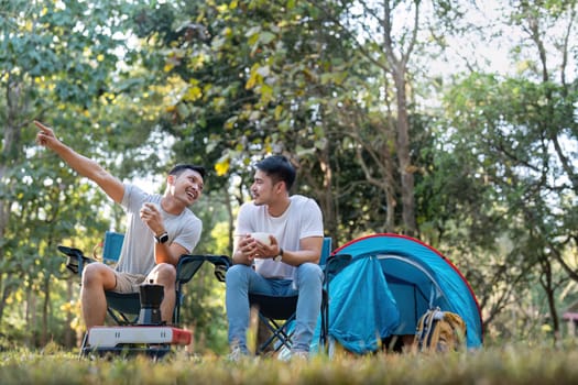 Male gay couple asian traveling with tent camping outdoor and various adventure lifestyle hiking active summer vacation. drinking coffee and talking together.