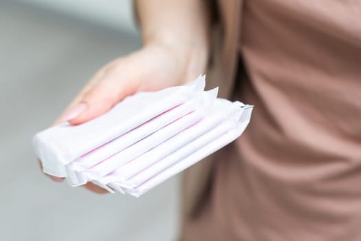 Young adult woman hand holding packs of sanitary towel on light background. Pastel color. Closeup. Empty place for text. High quality photo