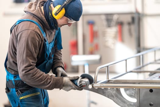 A tradesman wearing highvisibility workwear and ear muffs is grinding metal in an engineering workshop