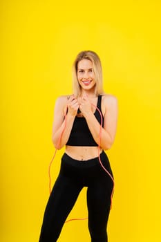 Fitness woman doing jumping exercises with a skipping rope on colorful yellow red background.