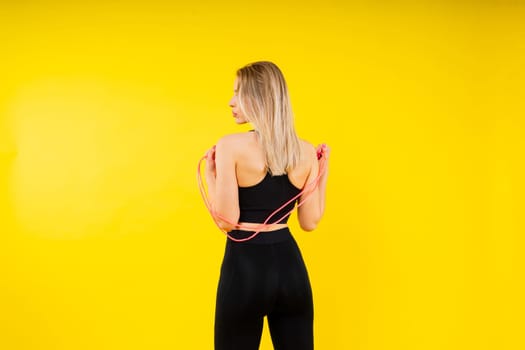 Fitness woman doing jumping exercises with a skipping rope on colorful yellow red background.