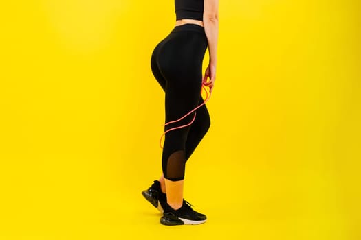 Fitness woman doing jumping exercises with a skipping rope on colorful yellow red background.