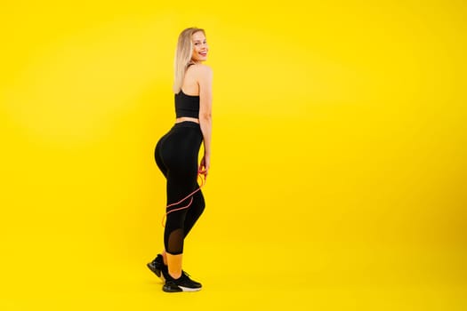 Fitness woman doing jumping exercises with a skipping rope on colorful yellow red background.