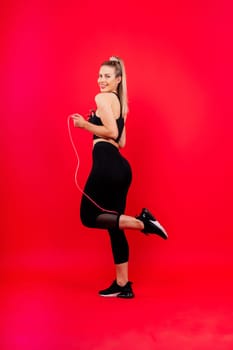 Fitness woman doing jumping exercises with a skipping rope on colorful yellow red background.