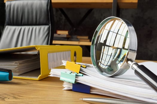 Magnifying glass on stack of financial reports as a symbol of an audit.