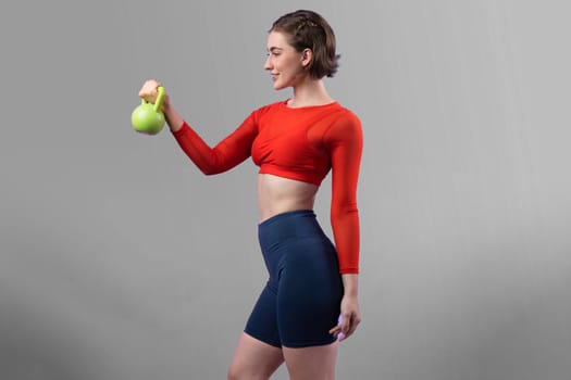 Full body length gaiety shot athletic and sporty woman with kettlebell for weight lifting as bodybuilding exercise in standing posture on isolated background. Healthy active and body care lifestyle