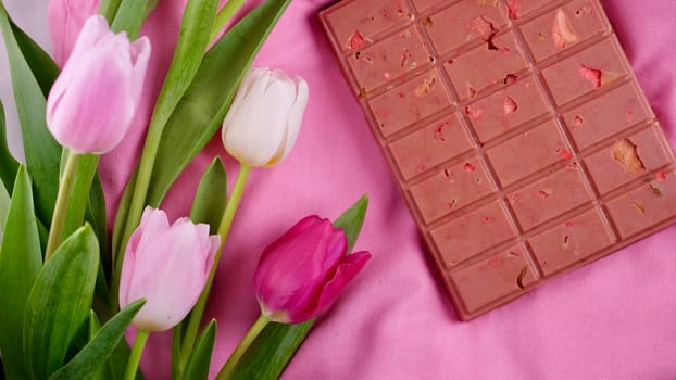 A bar of pink ruby chocolate with sublimated freeze-dried strawberries and almonds and spring tulip flowers . A dessert based on berries and nuts for International Women's Day, March 8, mother's day