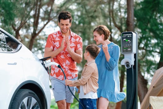 Outdoor adventure and family vacation camping in nature travel by eco friendly car for sustainable future. Lovely family recharge EV car with EV charging station in campsite. Perpetual