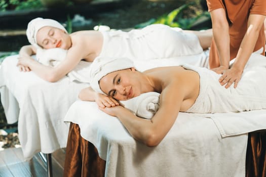 A portrait of two young attractive woman lie on bed during having back massage by a professional masseur at outdoor surrounded by peaceful natural environment. Healthy and beauty concept. Tranquility.