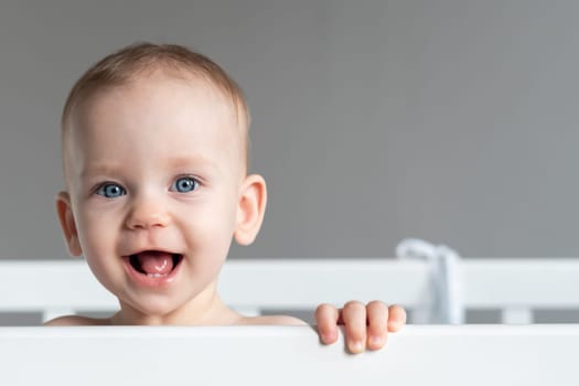 Portrait of one year old baby standing in a crib smiling
