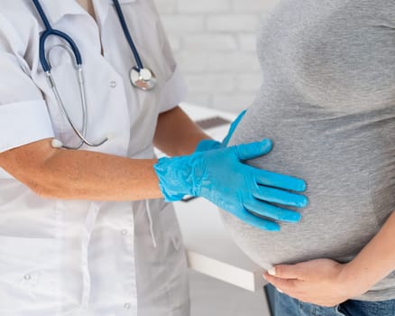 Pregnant woman visiting a doctor. Elderly Caucasian female gynecologist holds hands on the tummy of a pregnant patient