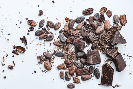 Chocolate and cacao concept. Cocoa beans and broken chocolate on white background. Top view copy space. Shallow dof.