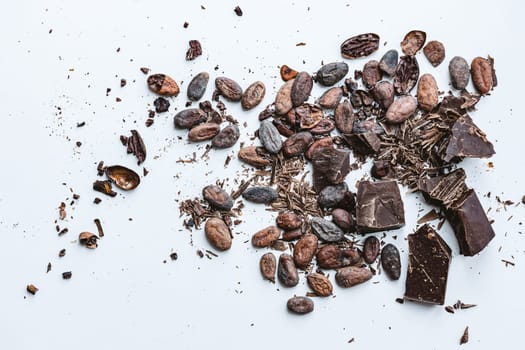 Chocolate and cacao concept. Cocoa beans and broken chocolate on white background. Top view copy space. Shallow dof.