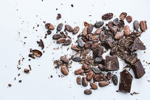 Chocolate and cacao concept. Cocoa beans and broken chocolate on white background. Top view copy space. Shallow dof.