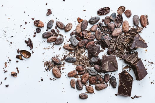 Chocolate and cacao concept. Cocoa beans and broken chocolate on white background. Top view copy space. Shallow dof.