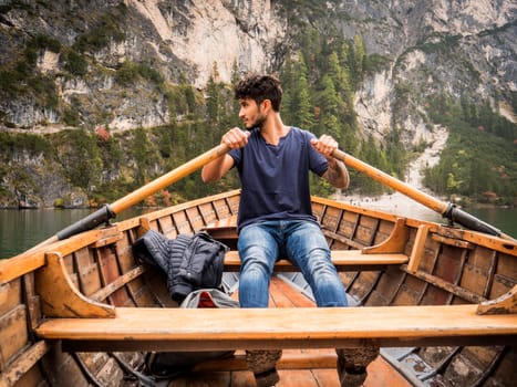 A man sitting in a boat on a lake. Photo of a man peacefully enjoying a boat ride on a serene lake amidst the breathtaking beauty of the Italian Dolomites