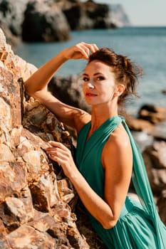 Woman green dress sea. Woman in a long mint dress posing on a beach with rocks on sunny day. Girl on the nature on blue sky background