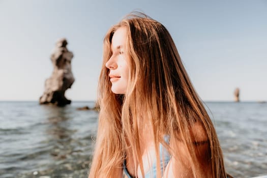 Close up shot of happy young caucasian woman looking at camera and smiling. Cute woman portrait in bikini posing on a volcanic rock high above the sea