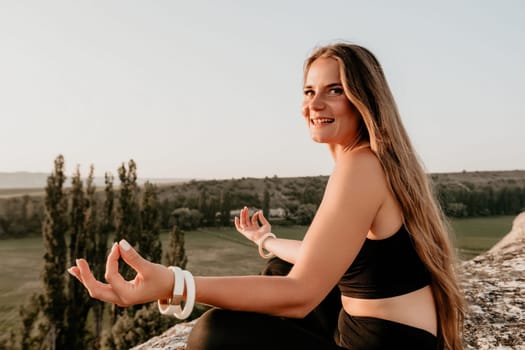 Well looking middle aged woman with long hair, fitness instructor in leggings and tops doing stretching and pilates on the rock near forest. Female fitness yoga routine concept. Healthy lifestyle.