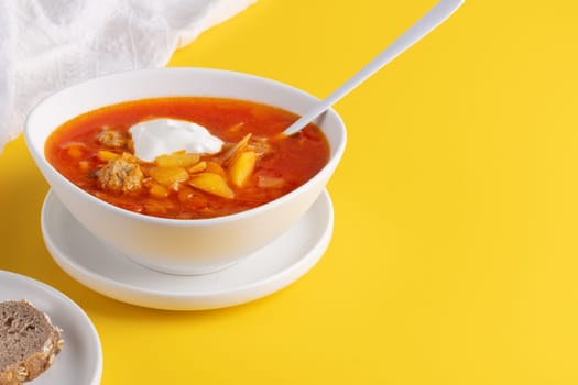 Red borscht in bowl on a yellow background, traditional dish that is cooked with broth. Copy space.